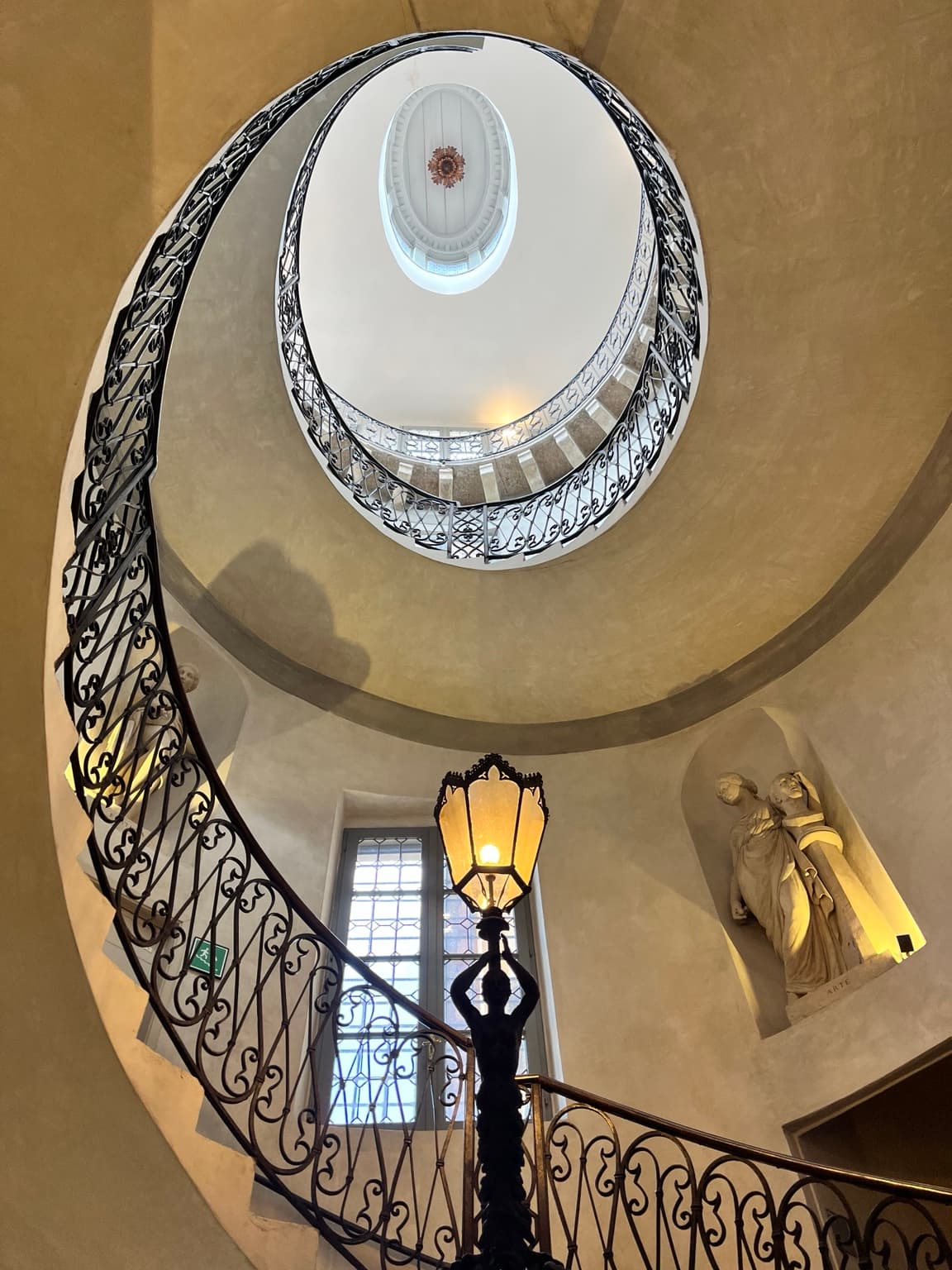 Temporary editorial reference, not Leighton House: curved staircase with ornate iron railings and a glowing lantern