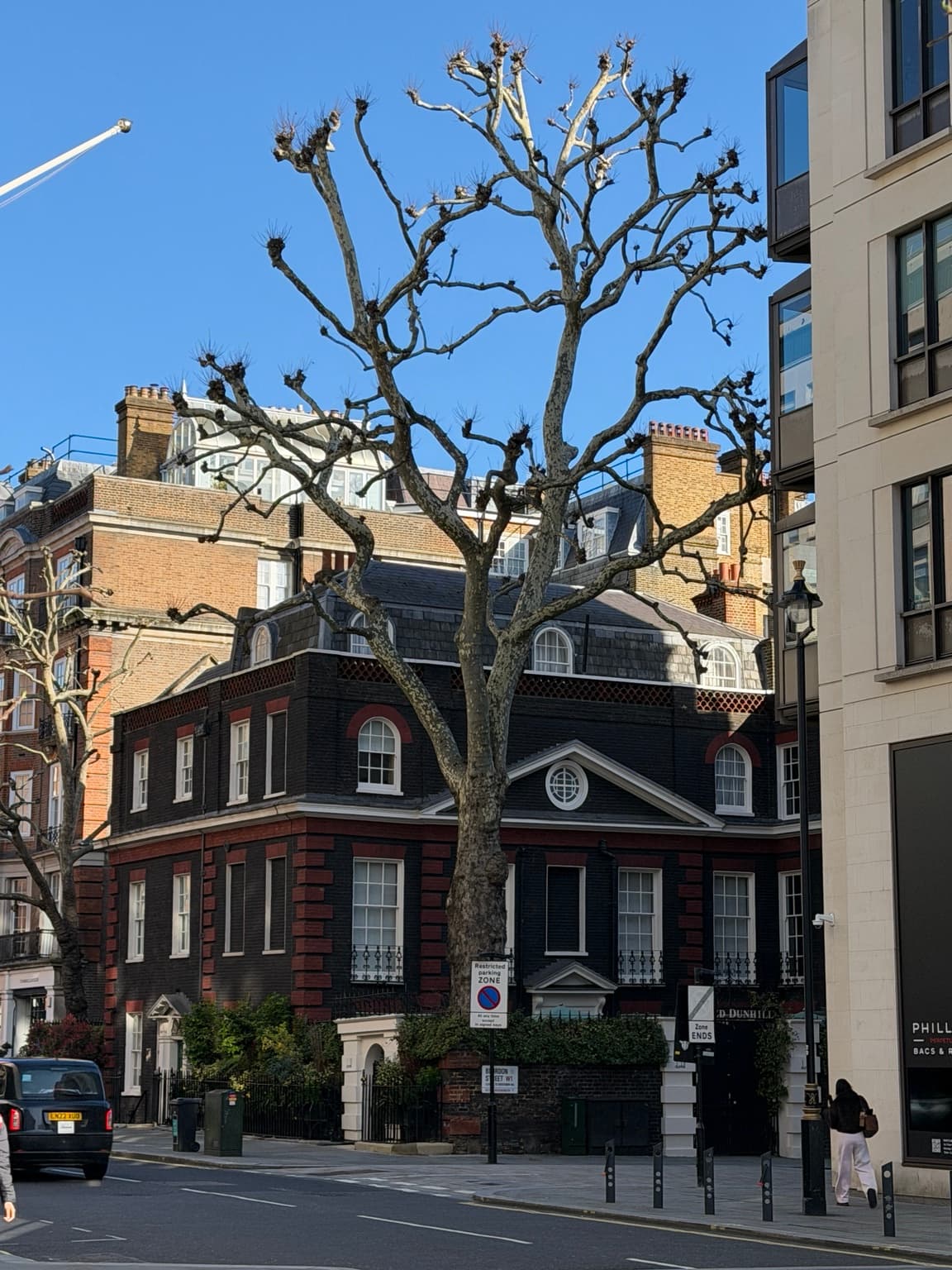 Editorial London streetscape with a leafless tree and a red-brick building beneath a blue sky; not a photograph of Middle Eight hotel