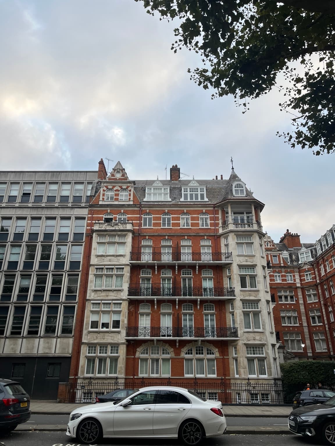 Editorial London street photograph of a red-brick building with pale stone window bays, wrought-iron balconies and parked cars; a city reference for The Resident Covent Garden