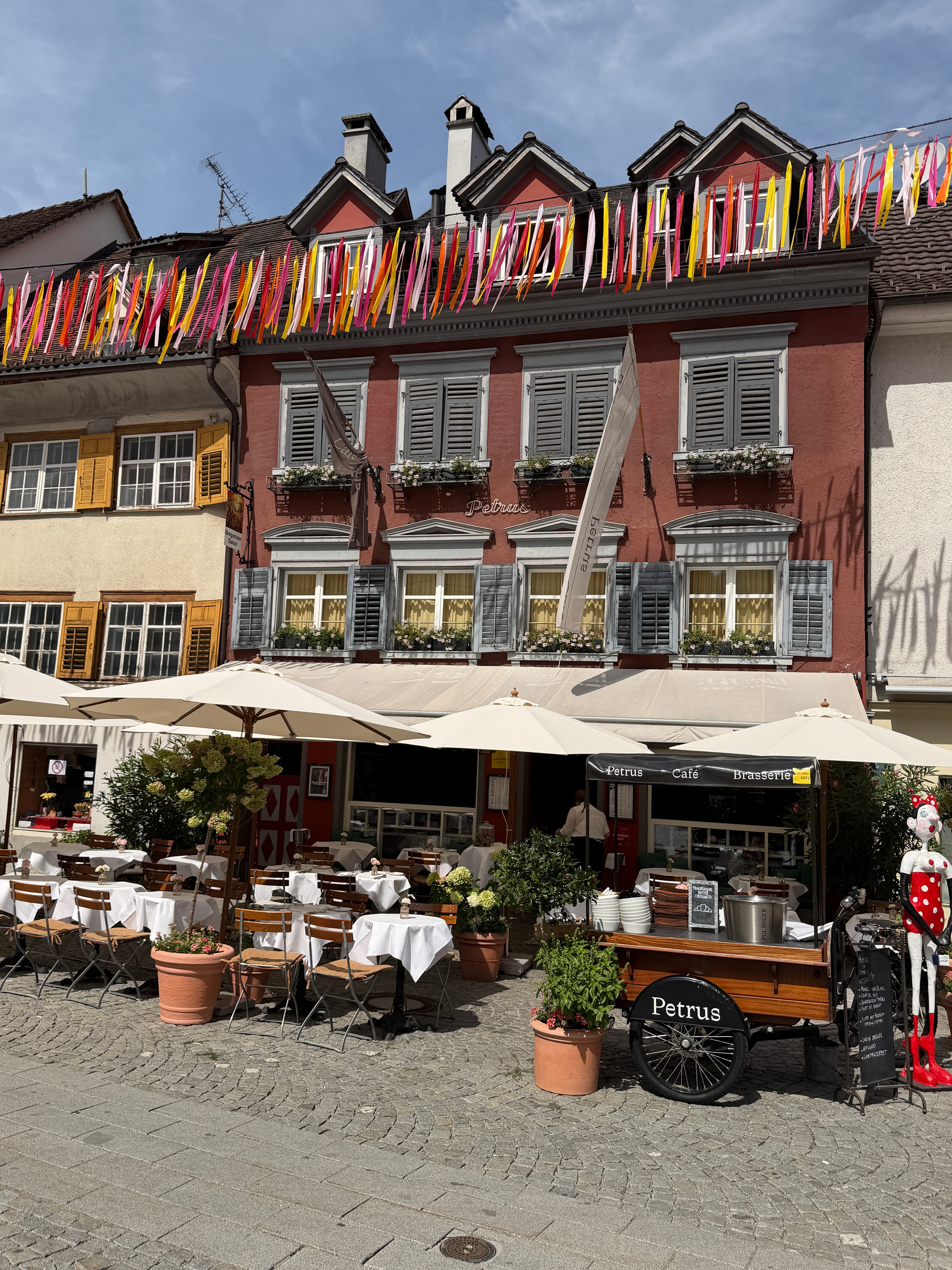 Original Opera Atlas photograph of Petrus Café Brasserie in Bregenz, showing its red façade, terrace and colourful festival ribbons