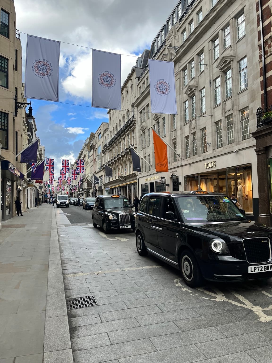 Black cabs on Bond Street beneath Union flags and coronation banners, with shopfronts along the pavement
