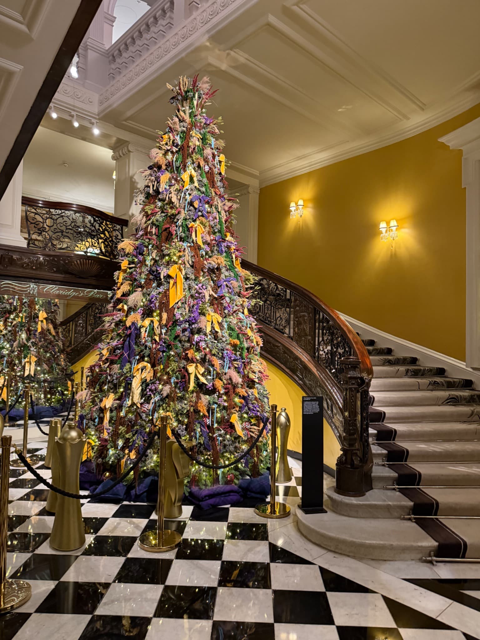 Christmas tree with colourful ribbons beside the sweeping staircase and black-and-white marble floor at Claridge’s
