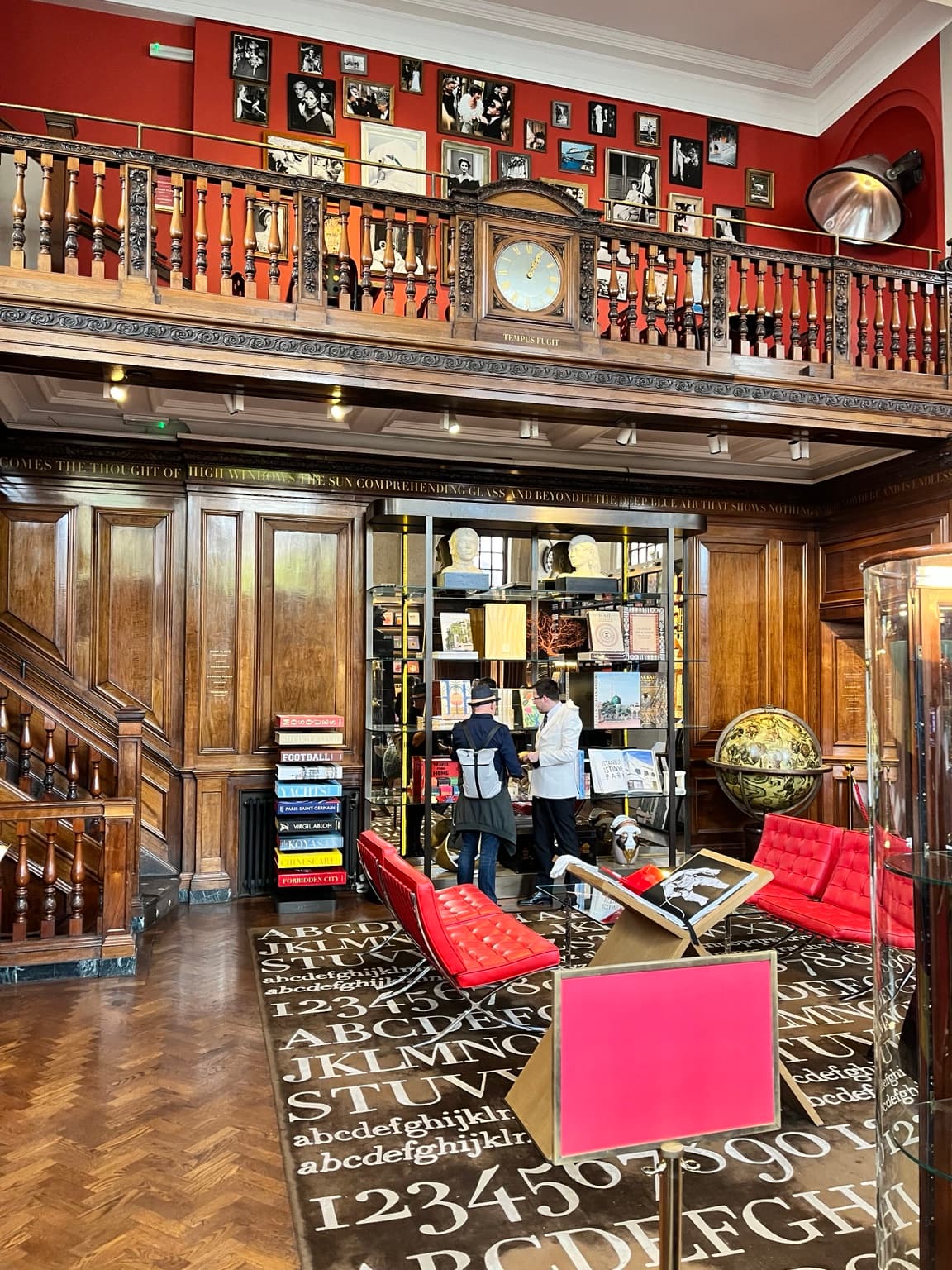Wood-panelled interior at Maison Assouline with a carved balcony, clock, books and red seating